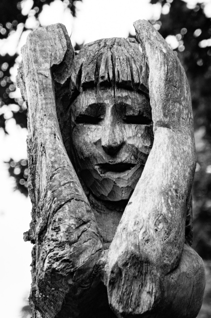 rough wooden carving of a person clutching their head with an anguished expression